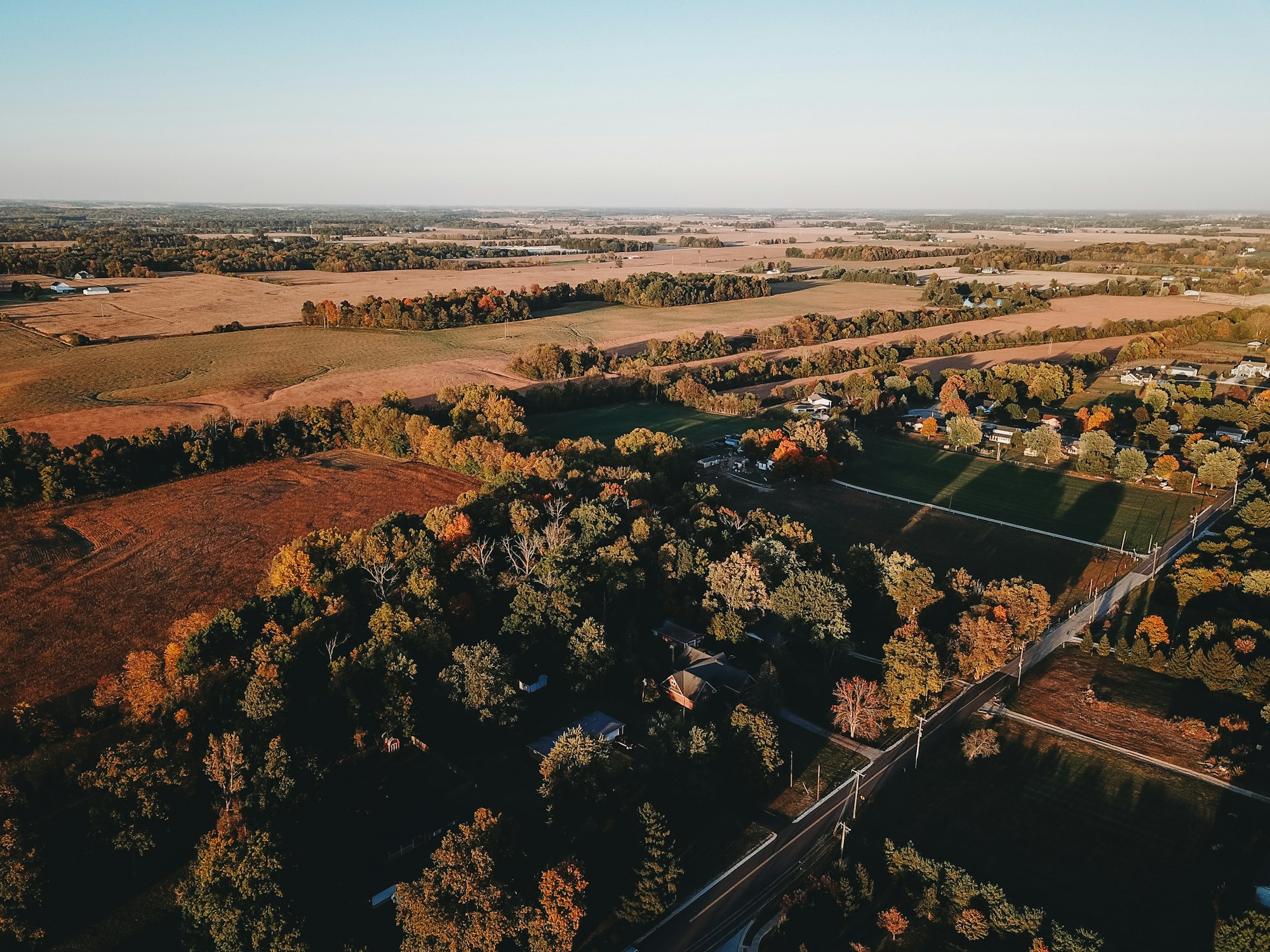 A small Indiana town meeting farmland at golden hour, from above
